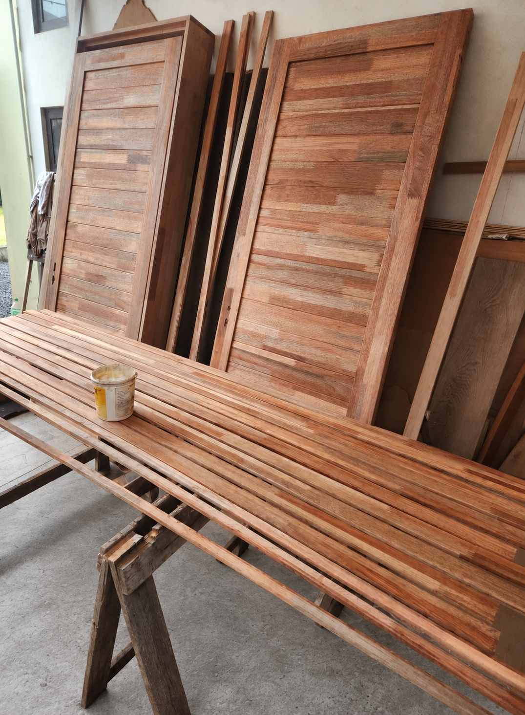 Portes en bois derrière un long ouvrage à lames posé sur des tréteaux dans un atelier