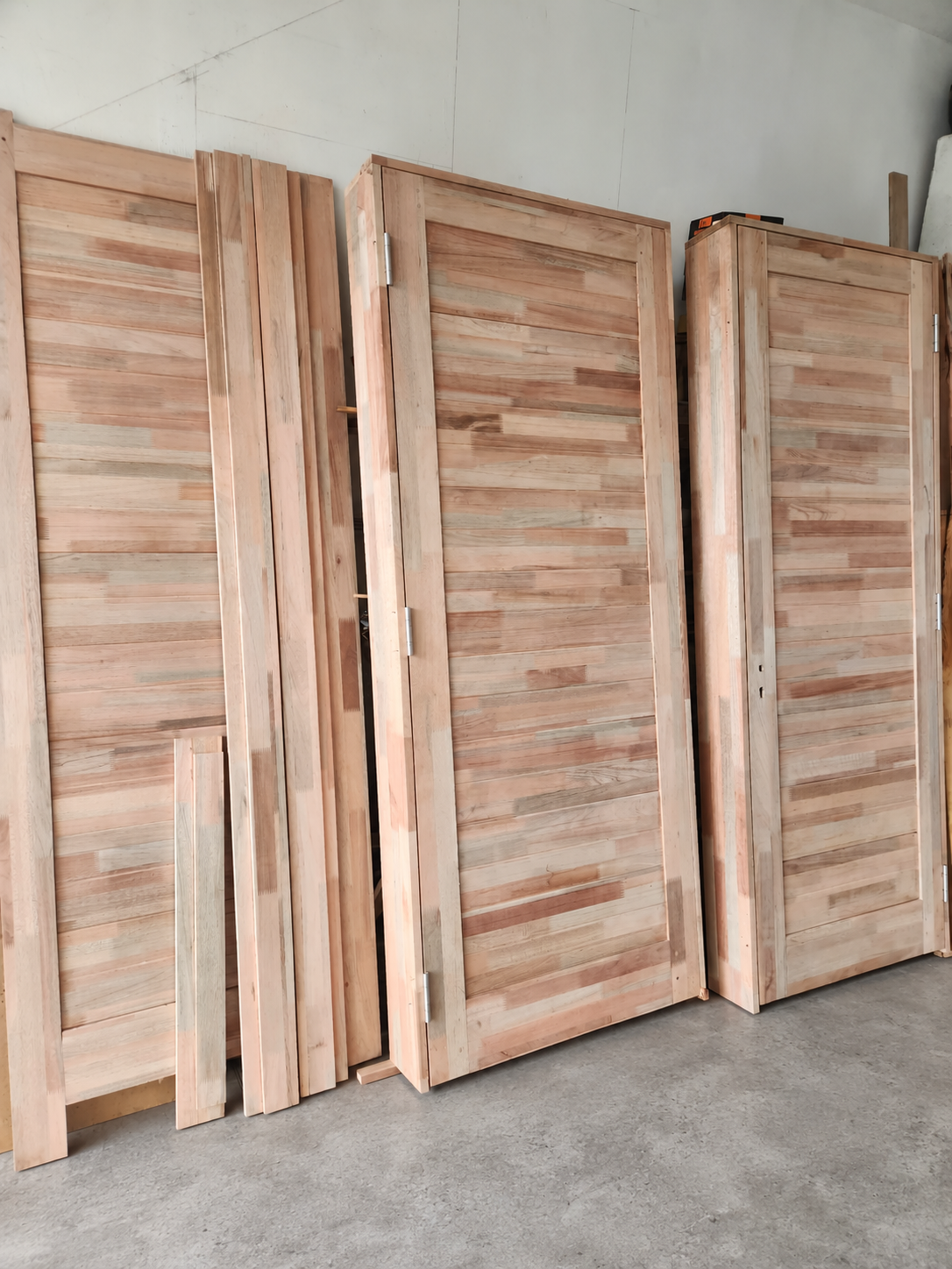 Portes en bois non finies et planches dressées sur un sol gris dans un atelier