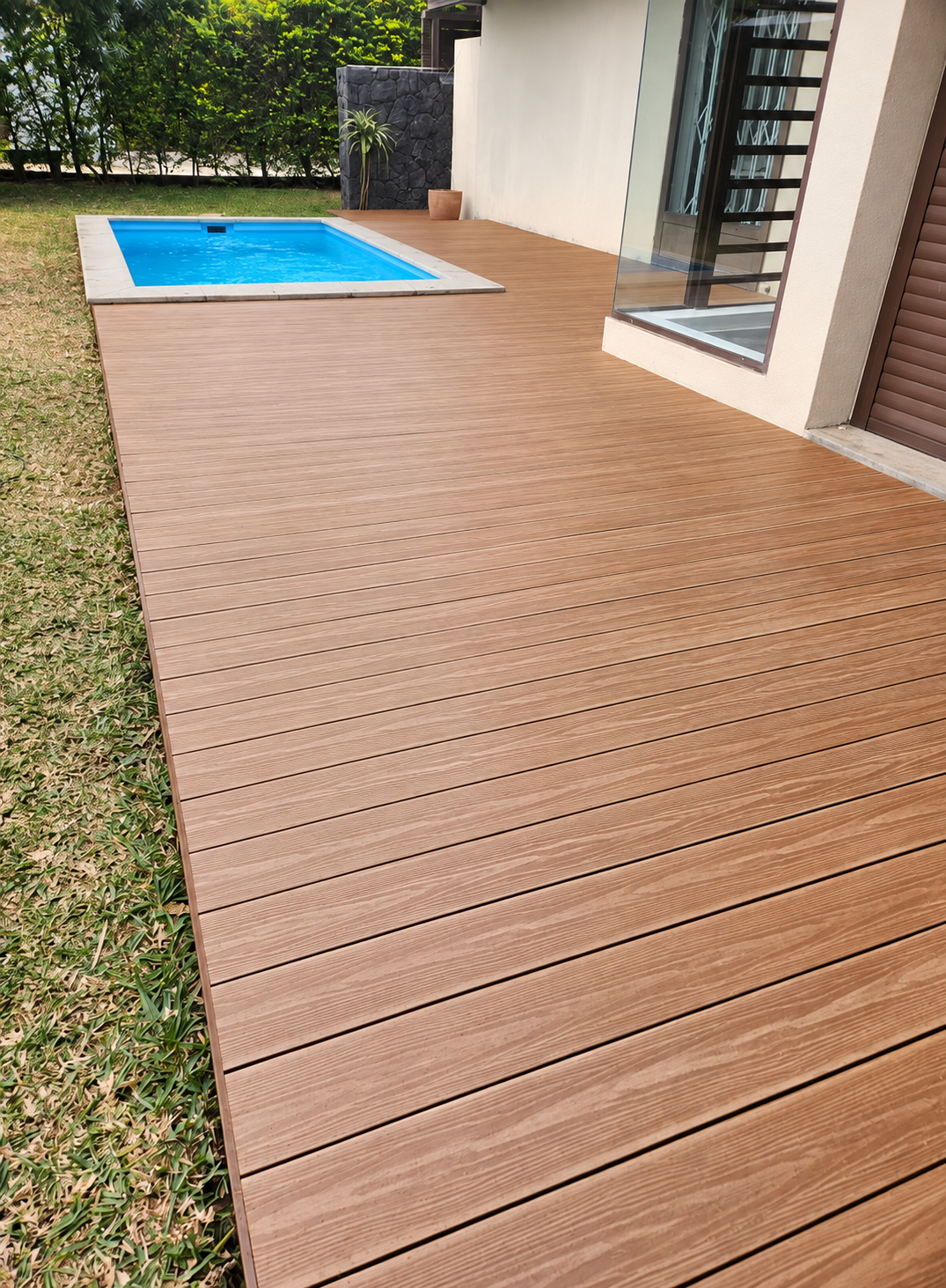 Terrasse en lames rainurées autour d’une piscine, devant une maison et un jardin